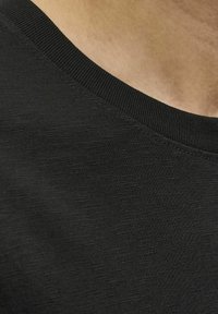 Camisa negra de manga corta con cuello redondo acanalado, que presenta una tela texturada y sutiles variaciones en el tono y el tejido.