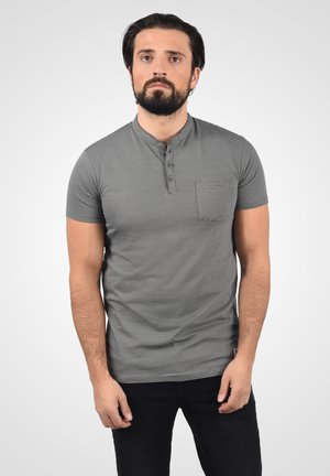 Camisa polo de manga corta a rayas grises y blancas con un cuello henley abotonado y un bolsillo en el pecho, confeccionada con un tejido suave.