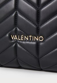 Svart skinnveske med et chevron-quiltet mønster. Gull "VALENTINO" logo fremhevet. Glatt tekstur og sofistikert design.