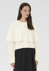 Fehér kötött pulóver rétegezett k�öpeny dizájnnal, gombos záródással és bordázott mandzsettával; puha tapintású és laza szabású.