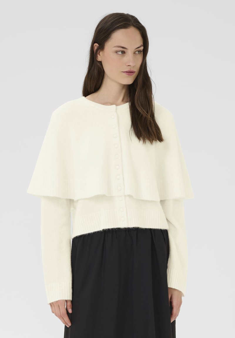 Fehér kötött pulóver rétegezett köpeny dizájnnal, gombos záródással és bordázott mandzsettával; puha tapintású és laza szabású.