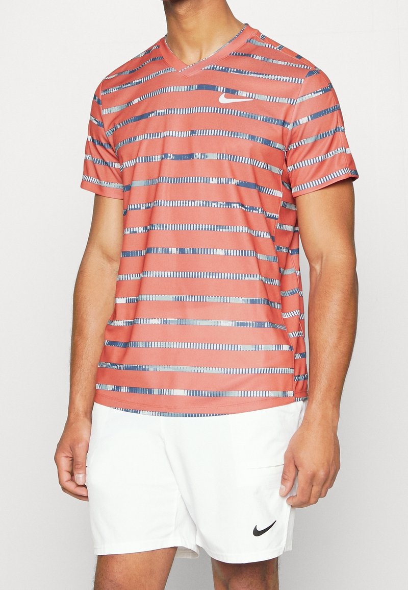 Camisa corta de manga roja de Nike con rayas horizontales en azul y plata. Diseño de cuello en V con un logotipo en el pecho. Material ligero.