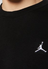 Gros plan d'une personne portant un t-shirt noir avec un logo en silhouette blanche d'un joueur de basket sautant et tenant un ballon au niveau de la poitrine.