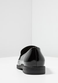 Scarpa in vernice nera con punta arrotondata e tacco basso e strutturato. Presenta una finitura liscia e cuciture sottili sul retro.