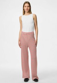 Haut sans manches blanc associé à un pantalon large rayé rouge et blanc. Le pantalon arbore une taille élastique et un tissu doux et texturé.