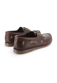 Zapatos náuticos de cuero marrón con ojales dorados, detalles cosidos y una suela de goma en tono marrón claro contrastante. Diseño de talón abierto para fácil uso.