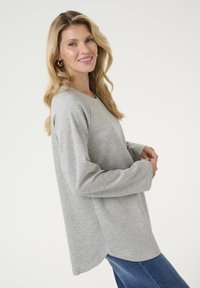 Polo gri cu mânecă lungă, cu decolteu rotund și croială lejeră. Textură moale, fante laterale, asortat cu blugi albaștri. Design minimalist.