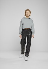 Felpa grigia corta con cappuccio, abbinata a pantaloni in pelle nera a vita alta e sneakers bianche. Texture lisce e design moderno.
