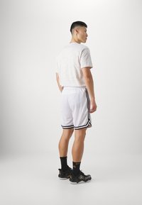 Camiseta gráfica blanca con un sutil patrón circular, combinada con shorts blancos que presentan franjas laterales negras. Zapatillas deportivas negras y calcetines.