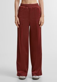 Maroon wide-leg pants made of smooth fabric with an elastic waistband, featuring front stitching details and a relaxed fit.