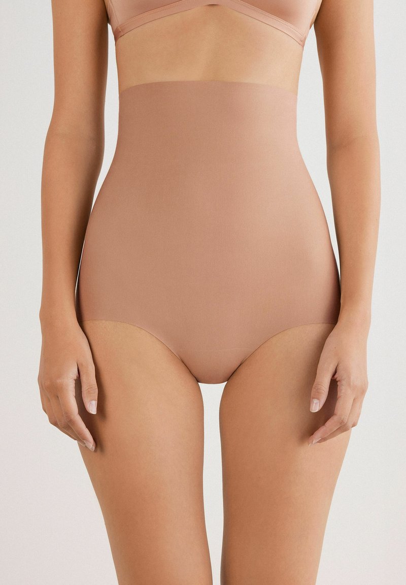 Högmidjade shapewear i ljusbeige, tillverkad av mjukt, stretchigt tyg. Har en sömlös design utan synliga kanter.