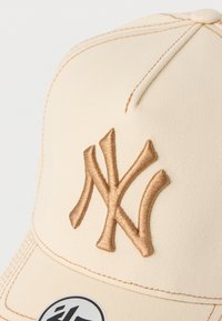Μπεζ καπέλο μπέιζμπολ με ανάγλυφο καφέ κεντημένο λογότυπο "NY", με ραμμένες λεπτομέρειες και κυρτό γείσο για δομημένο σχήμα.