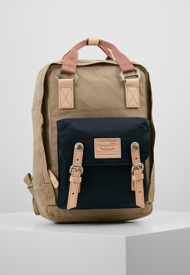Torebka plecak w odcieniach beżu i granatu o smukłym designie, z akcentami skórzanymi, regulowanymi paskami oraz przednią kieszenią zamykaną na klamry.