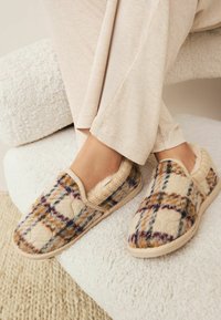 Chaussons en flanelle à motif écossais mélangé dans des tons de beige, marron et violet, avec une doublure en peluche et une semelle rembourrée pour le confort.