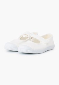 Zapatillas de lona blancas con punta redonda, aberturas laterales elásticas y una suela de goma blanca con un patrón de agarre texturizado.