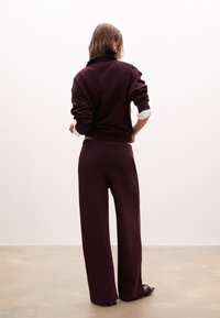 Completo in felpa color bordeaux e pantaloni a gamba larga, realizzato in tessuto morbido. Presenta un colletto alto, polsini elasticizzati e una vestibilità comoda.