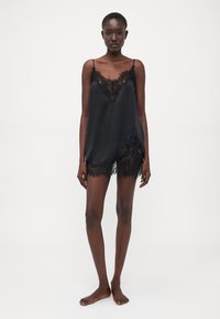 Svart sateng cami med justerbare stropper, blonde detaljer langs utringningen og hemsen, samt løssittende design. Ingen mønstre eller maskinvare.