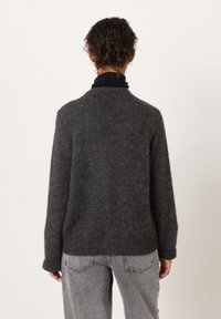 Gray, cozy wool sweater with long sleeves, ribbed hem, and a round neckline, worn over a black turtleneck. Plain texture, no patterns.