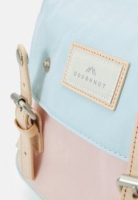 Backpack with a blue and pink fabric design, featuring a textured surface, silver hardware, and a beige label with "DOUGHNUT" text.