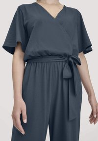 Dunkelgrauer Wickel-Overall mit kurzen Ärmeln, V-Ausschnitt, elastischem Taillenbund und einem gebundenen Akzentgürtel. Glatte Textur und lässige Passform.