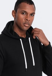 Sudadera negra de algodón con una textura suave, que cuenta con un cordón en blanco, bolsillo tipo canguro y puños acanalados.