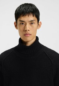 Schwarzer Fleecepullover mit Rollkragen, strukturierter Oberfläche, geripptem Kragen und Raglanärmeln, mit hohem Kragen für zusätzliche Wärme.