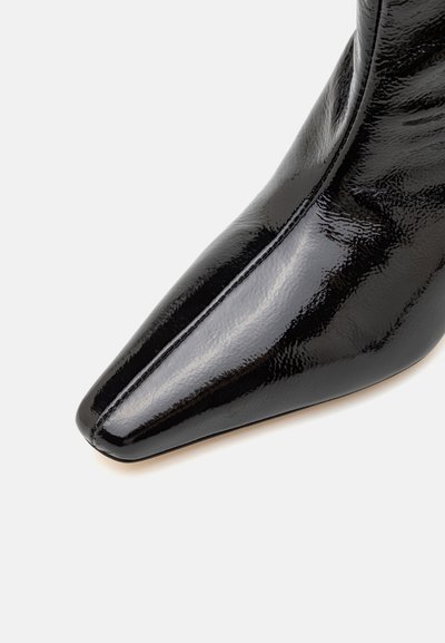 Must ylikoo mustast lakknahast jalanõu, millel on terav nina, sile tekstuur ja nähtav õmblusdetail külgõmblusel. Elegantne disain.