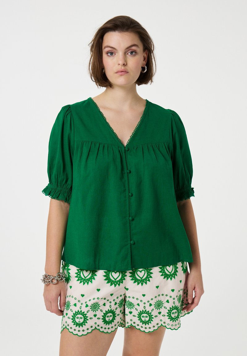 Groene linnen blouse met korte poff mouwen en een V-hals, voorzien van decoratieve knopen en bies. Gecombineerd met gestreepte crèmekleurige shorts.
