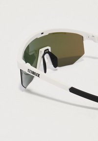 Γυαλιά ηλίου Bliz με λευκό σκελετό, πράσινους φακούς και μαύρες λεπτομέρειες. Έχουν σπορ σχέδιο και ρυθμιζόμενα μαξιλαράκια μύτης για άνεση.