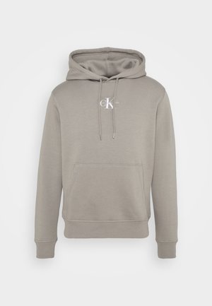 Helltaupefarbener Kapuzenpullover mit Kängurutasche vorne und weißem "CK"-Logo in der Mitte der Brust, mit verstellbarer Kapuze und gerippten Bündchen.