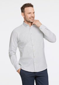 Camisa abotonada en gris claro y rayas blancas, con cuello, mangas largas y un detalle de bolsillo sutil. La tela parece suave.