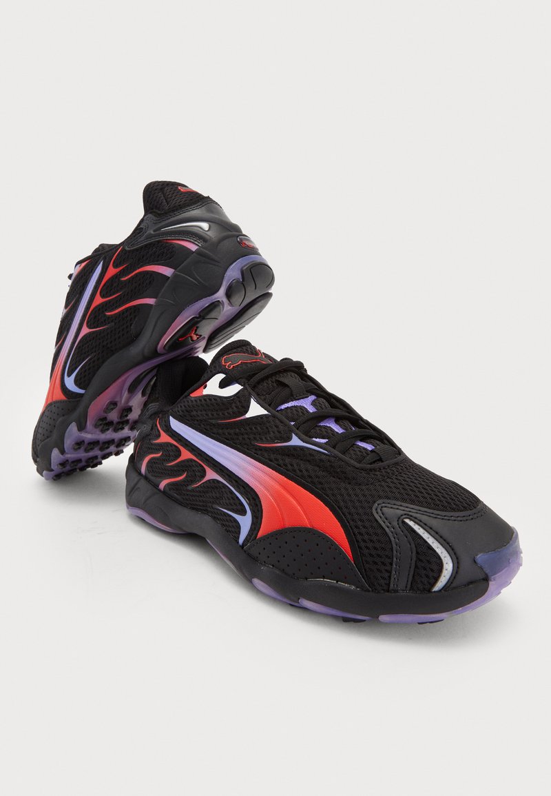 Zapatillas deportivas negras con acentos rojos y morados. Material de malla, con diseños similares a llamas. Suelas redondeadas con patrones de agarre texturizados.