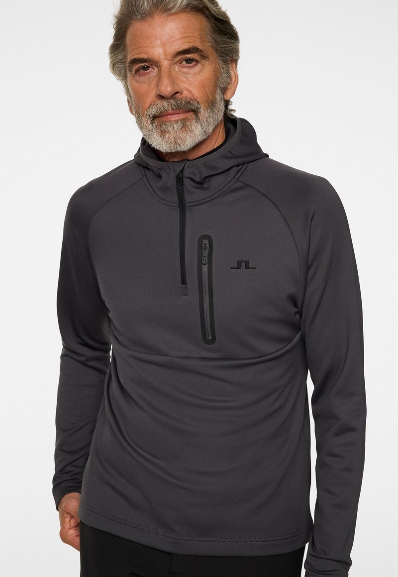 Dunkelgrauer Pullover mit Kapuze, ausgestattet mit einer mit Reißverschluss versehenen Brusttasche und dezentem Logo. Hergestellt aus glattem, elastischem Stoff mit einer figurschmeichelnden Passform.