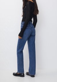 Jeans de mezclilla azul de tiro alto con corte recto, diseño de cinco bolsillos y textura suave. Lucidos con una blusa negra ajustada de manga larga y mocasines.