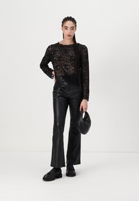 Black lace long-sleeve top over black faux leather flared pants, paired with black flat shoes and a small black handbag.