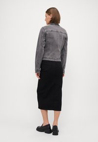 Veste en denim gris au design ajusté, avec des coutures visibles et un col. Assortie à une jupe noire à mi-mollet et des chaussures noires épaisses.