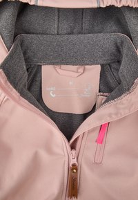 Light pink jacket with a grey fleece interior, featuring a front zipper, pink zipper accent, and a label for name and contact details.