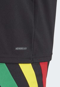 Zwarte sportshirt met de tekst "AEROREADY". Heeft meerkleurige diagonale strepen in groen, geel en rood aan de onderzijde. Gladde textuur.