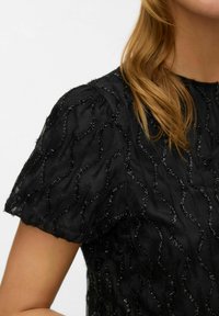 Czarny top z tkaniny z haftem przypominającym fale, z teksturowanymi akcentami. Krótkie rękawy i miękki, lekki materiał.