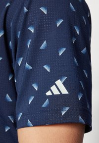 Námořnické sportovní tričko s malými modrými trojúhelníkovými vzory; strukturovaná látka; bílý logo Adidas na rukávu; krátké rukávy a kulatý výst�řih.