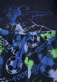 Niebieska i czarna koszulka z grafiką piłkarza; pasujące szorty mają zielone i niebieskie plamy, nadruki piłek nożnych oraz elastyczny pas.