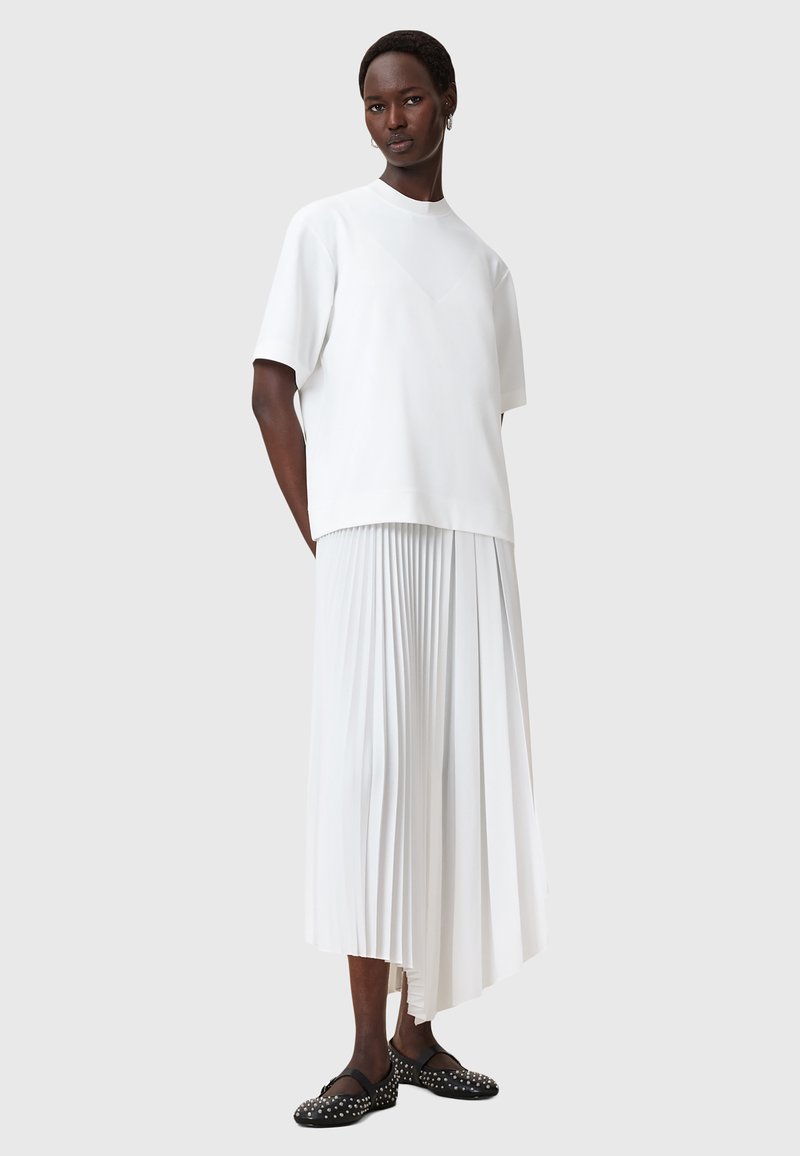 Top bianco a maniche corte abbinato a una gonna bianca fluida e plissettata, che mette in risalto texture morbide. Completa il look un paio di ballerine nere con dettagli borchiati.