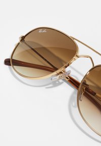 Gold aviator sunglasses with brown lenses, featuring a metal frame, clear nose pads, and brown tortoiseshell temple accents.