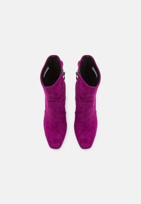Botas de ante fucsia hasta el tobillo con punta afilada, textura suave y cremallera lateral para el cierre. Diseño estructurado y caña de altura media.