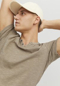 Taupe, kortærmet t-shirt med struktureret overflade og to-knaps halsudskæring. Båret med en lyse farvet cap, der fremhæver en afslappet pasform.