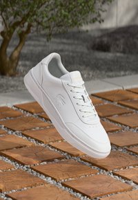 White lace-up sneaker made of smooth leather with a minimalist design, featuring perforations on the toe and a rubber sole.