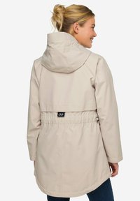 Ljusbeige vattentålig jacka med huva, cinchad midja och slits på baksidan. Slät textur, långa ärmar och elastiska detaljer.