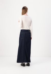 Tummansinisestä denimmaxihameesta, joka on suoran muotoinen ja jossa on kaksi takataskua sekä musta vyötärö, on yhdistetty tiukkaan valkoiseen toppiin.