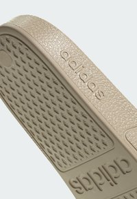 Semelle de sandale slide beige Adidas avec motif de grip texturé et logo Adidas embossé sur le côté et le dessous.