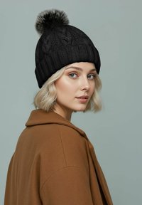 Black knitted beanie with a ribbed design and a fluffy pom-pom on top, paired with a brown coat. Smooth texture, close-fitting shape.